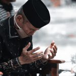 Man in Black Leather Jacket and Black Knit Cap Sitting on Brown Wooden Chair