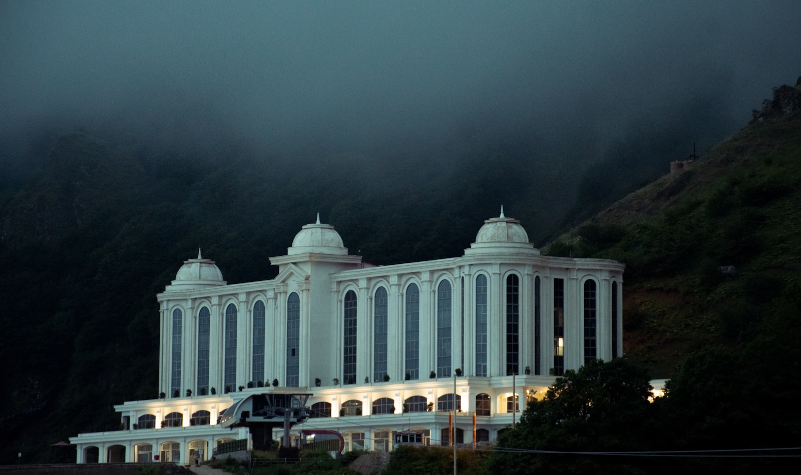 A large white building sits in front of a foggy mountain.